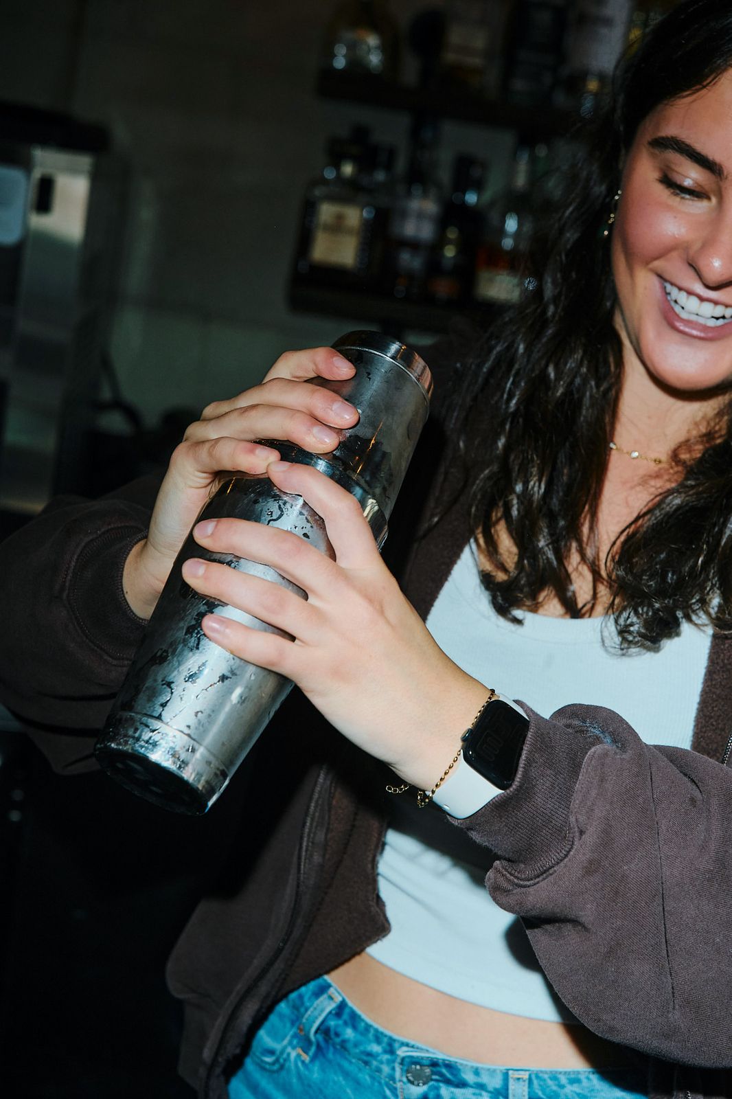 A smiling bartender shaking a cocktail behind the bar